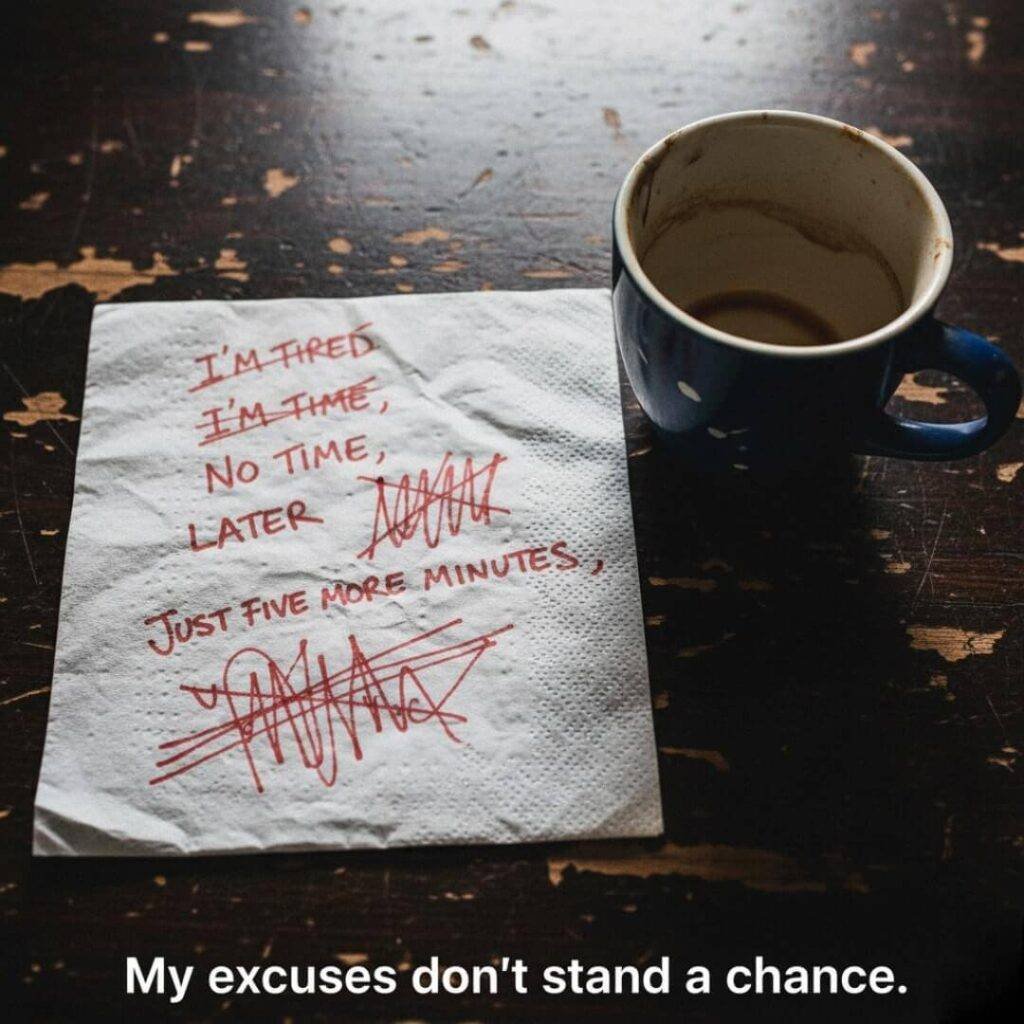 A close-up, harshly lit photo of a crumpled napkin with "I'M TIRED," "NO TIME," "LATER," and "JUST FIVE MORE MINUTES" scribbled out in red pen, next to a chipped, empty coffee mug on a wooden surface.