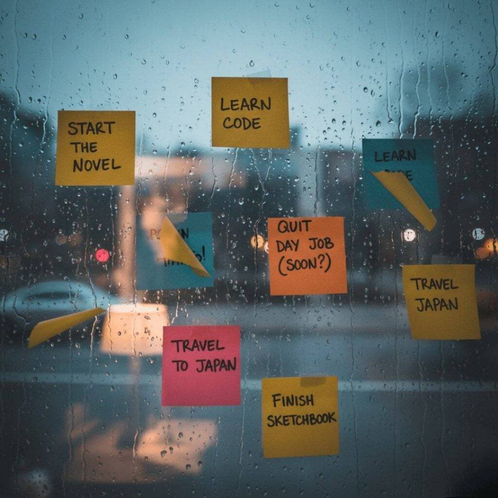 Rain-streaked window with sticky notes outlining fragmented dream goals like "START THE NOVEL" and "TRAVEL JAPAN", viewed from an intimate, inside perspective.