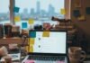 Personal Branding Power: Skyrocket Your Motivation Today! A cluttered desk with a laptop displaying a blog draft, a "Hustle" mug, and numerous sticky notes, set against the blurry backdrop of a Seattle window.
