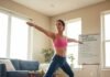 Home Workout Motivation: How to Push Through Slumps A woman in activewear performs a warrior pose on a yoga mat in a sunny living room, with a dog lying beside her and a whiteboard titled "Home Workout Inspiration" in the background.